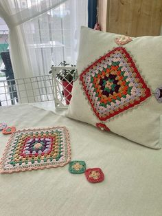 two crocheted squares are laying on a bed next to a pillow and some other items