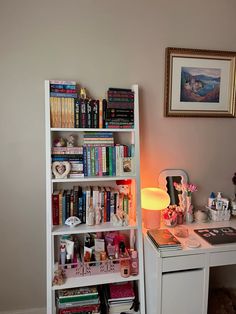 a white book shelf filled with lots of books next to a desk and lamp on top of it