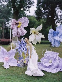 a woman in a white dress standing next to purple and blue flowers on the grass