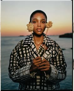 a woman standing next to the ocean holding two flowers