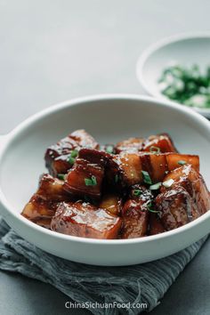 tofu with sauce in a white bowl on a gray cloth next to another dish