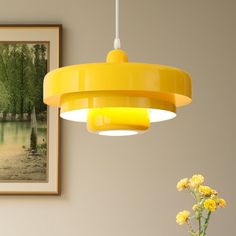 a yellow light hanging over a table next to a vase with flowers in it and a painting on the wall