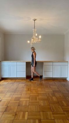 a woman is walking in an empty room with chandelier hanging from the ceiling