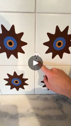 a person pointing at some decorative tiles on the wall with blue and brown circles around them