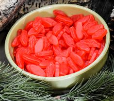 a bowl filled with red candy sitting on top of a table next to pine cones