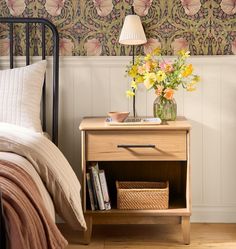 a nightstand with flowers on it next to a bed