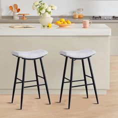 two stools in the middle of a kitchen with white counter tops and wooden floors