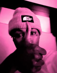 a man wearing a beanie covering his face in front of a pink light with the north face logo on it