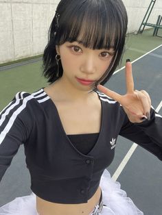 a woman in a black top and white tutu is giving the peace sign while standing on a tennis court