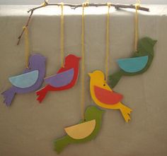 three colorful birds hanging from strings on a gray wall with yellow, green, blue and red colors