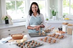 a woman in an apron preparing food on top of a kitchen counter next to baking trays