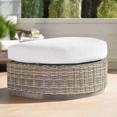 a round wicker ottoman sitting on top of a wooden table next to a plant