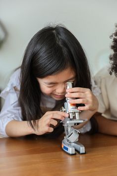 two girls looking through microscopes at something on the table with one girl holding it in her hands