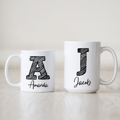 two white coffee mugs with the letters j and person written in black on them