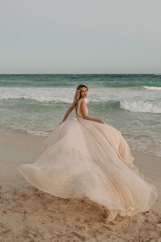 a woman in a long dress is sitting on the beach