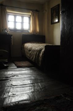 a dark room with a bed, dresser and window