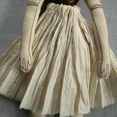 the doll is wearing a white dress with brown trims on it's arms