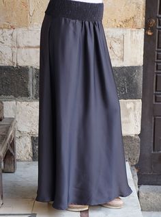 a woman wearing a long skirt standing in front of a stone wall with her hands on her hips