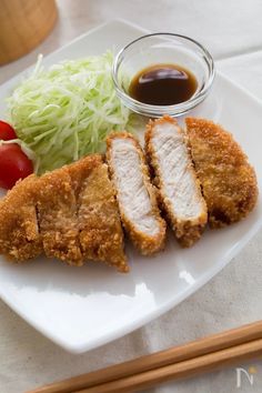 a white plate topped with meat and veggies next to chopsticks on a table