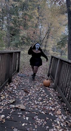 a person wearing a mask walking across a bridge with leaves on the ground and trees in the background