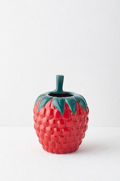 a red ceramic fruit with green leaves on it's top sitting on a white surface