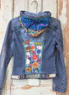 an old jean jacket with flowers on it hanging from a wooden hanger in front of a door