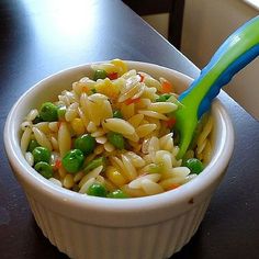 a white bowl filled with pasta and peas on top of a wooden table next to a window