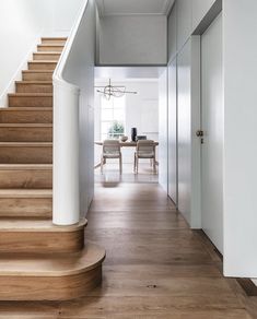 a wooden staircase leading up to a dining room and living room area with white walls