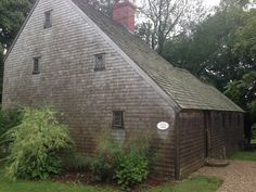 an old wooden building in the middle of some trees and bushes with a brick chimney