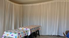 two tables with colorful tablecloths sit in front of a white curtained wall