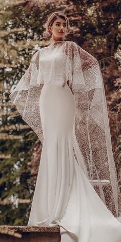 a woman wearing a white wedding gown and veil standing in front of trees with her hands on her hips