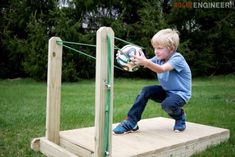 a young boy holding a soccer ball on top of a wooden structure in the grass