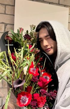 a man holding a bouquet of flowers in front of his face and wearing a hoodie