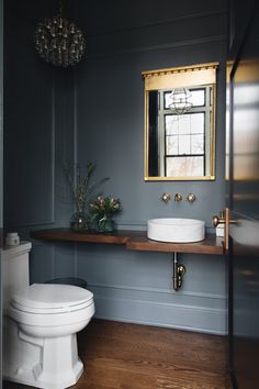 a white toilet sitting next to a sink in a bathroom under a mirror and a chandelier