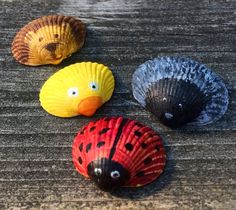 three seashells with faces painted on them sitting on a wooden surface, one is yellow and the other two are red