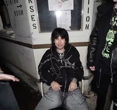 a young man sitting in a chair next to another person with his hand on his hip