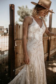 a woman in a white dress and cowboy hat leaning against a fence with her hand on her hip