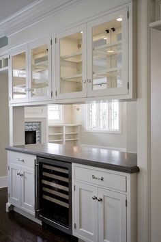 an empty kitchen with white cabinets and black counter tops, including a wine cooler in the center