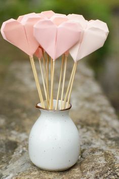 pink origami hearts in a white vase with sticks sticking out of it's top