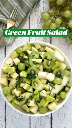 green fruit salad in a white bowl with grapes and kiwis on the side