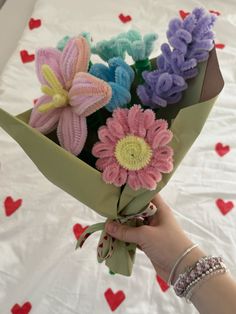 a hand holding a bouquet of flowers on top of a white bed covered in hearts