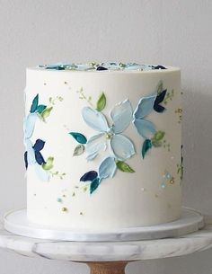 a white cake with blue and green flowers on it sitting on top of a wooden stand