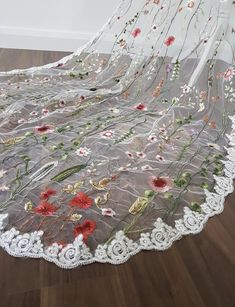 a white lace with red flowers on it sitting on top of a hard wood floor