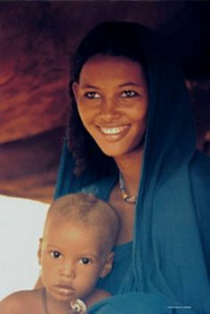 a woman holding a child in her arms and smiling at the camera while wearing a blue shawl