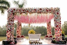 an outdoor wedding setup with pink flowers and greenery hanging from the ceiling, surrounded by white couches