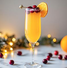 an orange and cranberry cocktail garnished with cherries on a table