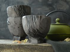 two gray vases sitting next to each other on top of a wooden table with a green teapot in the background