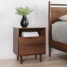 a bed with a nightstand next to it and a vase on top of the night stand