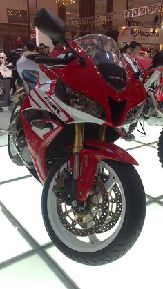 a red and white motorcycle on display in a building with people looking at the bikes