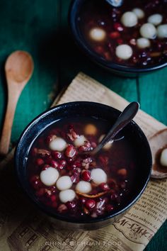 two black bowls filled with soup on top of a wooden table next to spoons